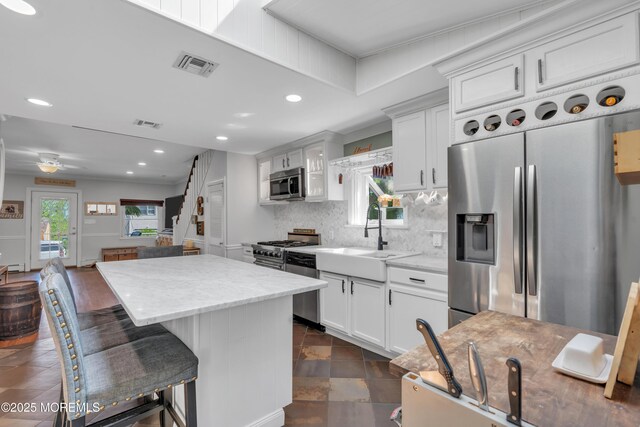kitchen with appliances with stainless steel finishes, a sink, backsplash, a kitchen island, and visible vents
