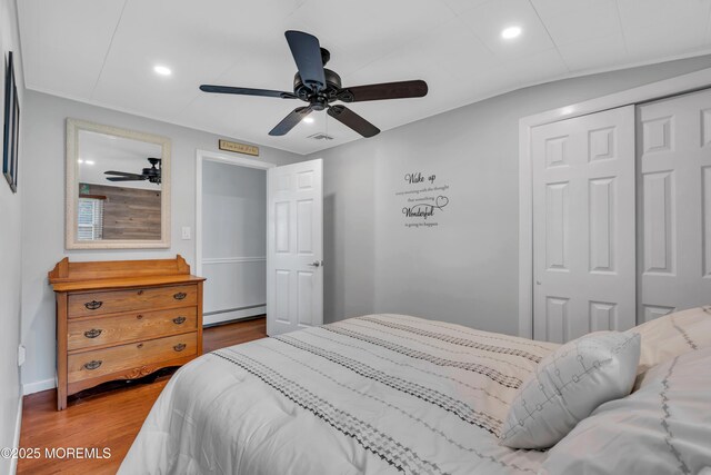 bedroom featuring ceiling fan, recessed lighting, wood finished floors, a baseboard radiator, and a closet