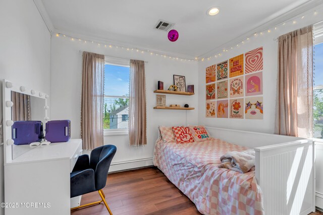 bedroom featuring multiple windows, a baseboard heating unit, wood finished floors, and visible vents