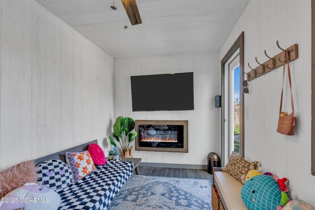 living room featuring a glass covered fireplace, wood finished floors, and wooden walls