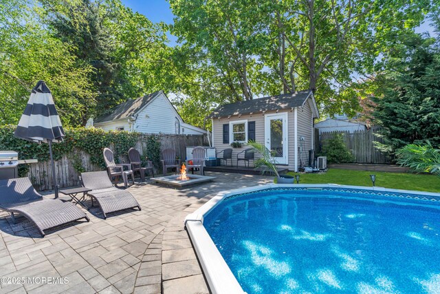 view of swimming pool featuring a fenced in pool, a fenced backyard, an outbuilding, a patio, and a fire pit