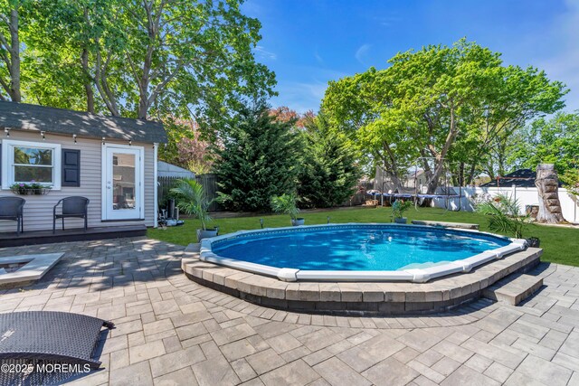 view of swimming pool with a fenced backyard, a trampoline, a lawn, and a patio