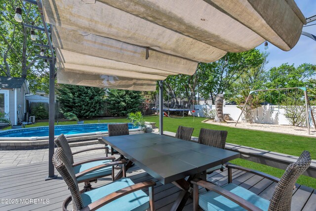 wooden deck featuring a trampoline, an outdoor structure, a fenced backyard, a shed, and a yard