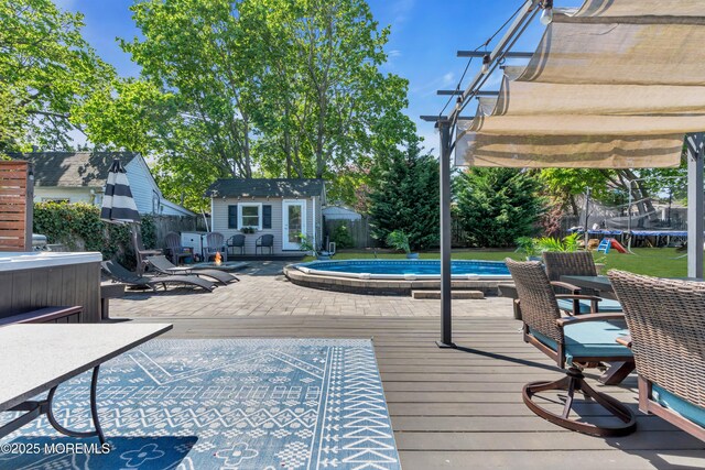 wooden deck featuring a fenced backyard, an outdoor structure, a trampoline, and a pool