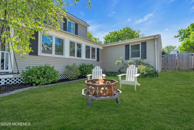 back of house featuring a lawn, fence, and a fire pit