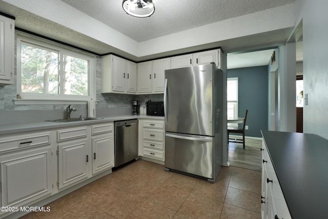 kitchen with a textured ceiling, white cabinetry, tasteful backsplash, a sink, and appliances with stainless steel finishes