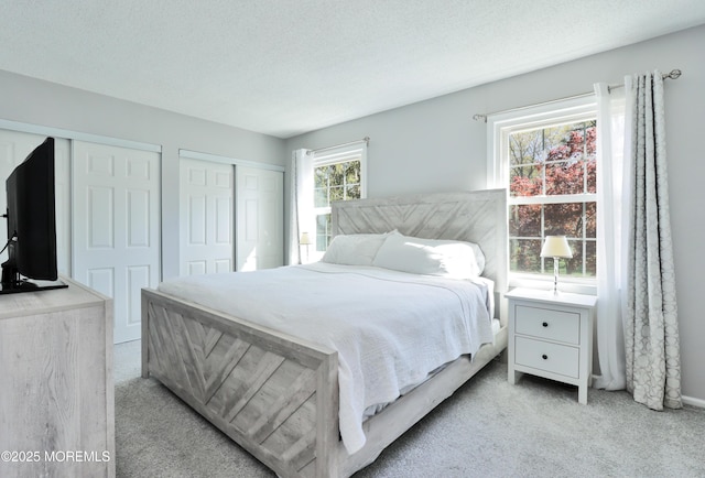 bedroom with light colored carpet, baseboards, a textured ceiling, and two closets