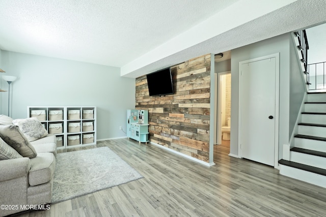 living room with stairway, a textured ceiling, baseboards, and wood finished floors
