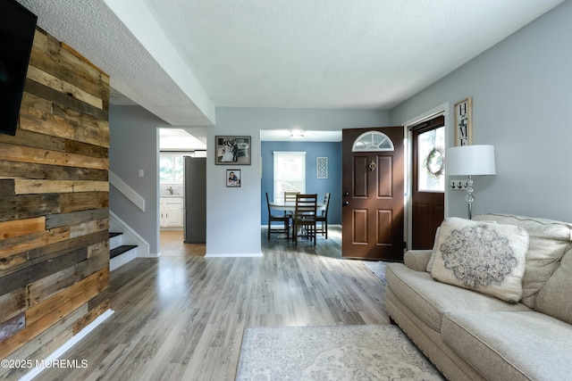 living area featuring light wood-type flooring, a textured ceiling, baseboards, and stairway