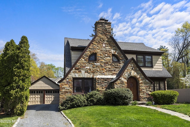 tudor home featuring an attached garage, a chimney, stone siding, and a front lawn