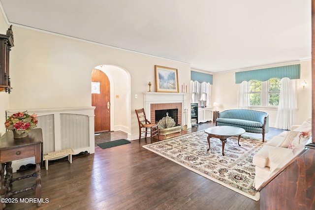 living area with crown molding, arched walkways, a brick fireplace, and wood finished floors
