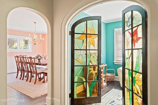 entryway with crown molding, wood finished floors, baseboards, arched walkways, and a notable chandelier