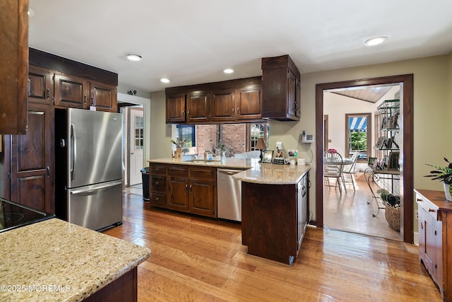 kitchen featuring light stone countertops, dark brown cabinets, a peninsula, stainless steel appliances, and light wood-style flooring