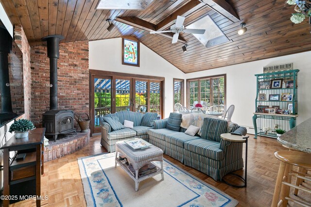 living area featuring wood ceiling, plenty of natural light, a ceiling fan, a skylight, and a wood stove