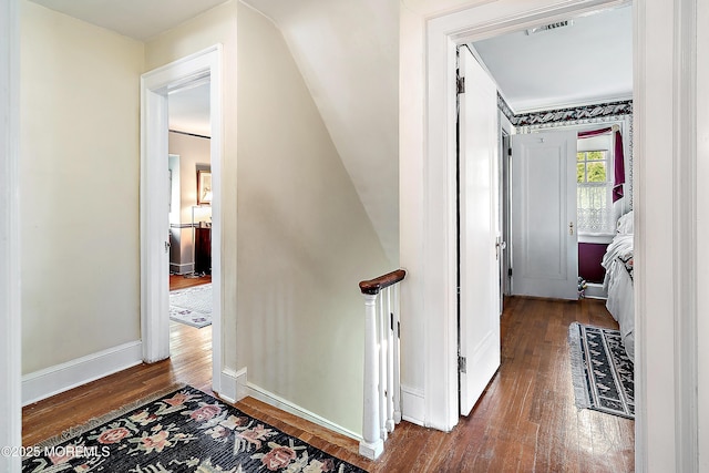hallway with baseboards, visible vents, and hardwood / wood-style flooring