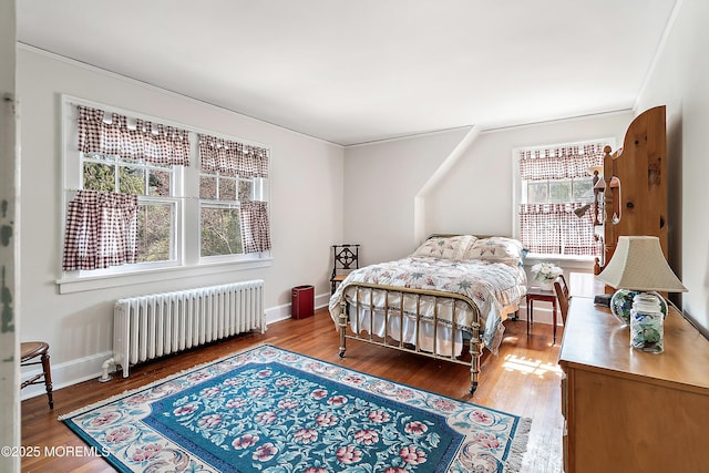 bedroom featuring baseboards, multiple windows, wood finished floors, and radiator