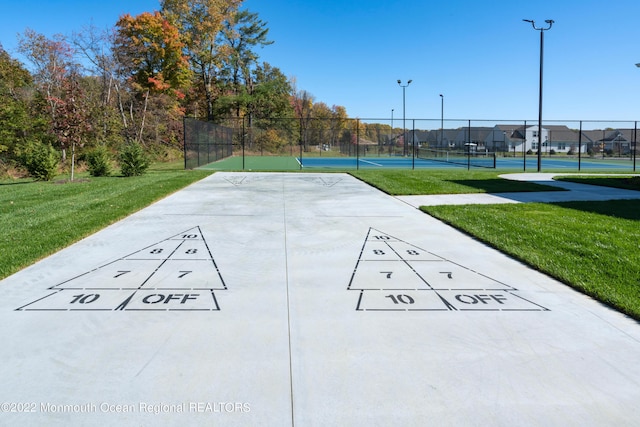 view of property's community featuring a lawn, shuffleboard, a tennis court, and fence