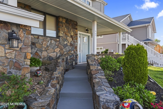 doorway to property with a porch, roof with shingles, and stone siding
