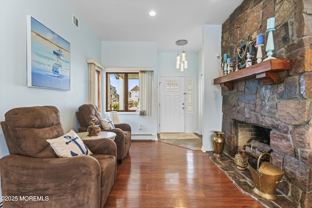 living area featuring a fireplace, baseboard heating, hardwood / wood-style flooring, and visible vents