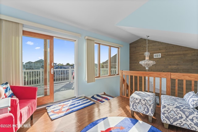 living area featuring wooden walls, vaulted ceiling, wood finished floors, and visible vents