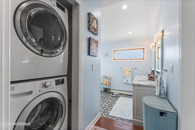 clothes washing area featuring laundry area, stacked washer and dryer, wood finished floors, baseboards, and a baseboard heating unit