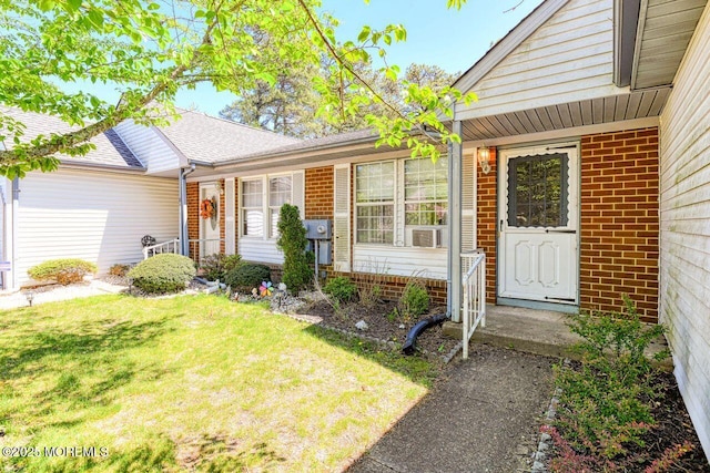 entrance to property featuring a shingled roof, a yard, and brick siding
