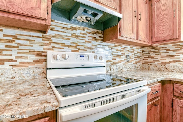 kitchen featuring brown cabinetry, white electric range oven, light countertops, under cabinet range hood, and backsplash