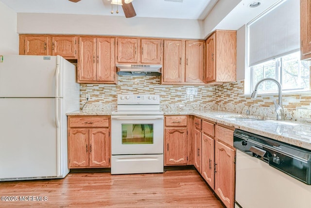 kitchen with decorative backsplash, light stone countertops, a sink, under cabinet range hood, and white appliances