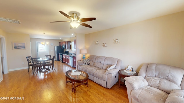living area featuring baseboards, visible vents, light wood-style flooring, and ceiling fan with notable chandelier