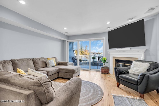living area featuring recessed lighting, visible vents, a glass covered fireplace, and light wood-style floors