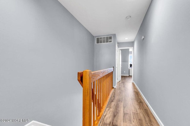 hall featuring visible vents, baseboards, wood finished floors, and an upstairs landing