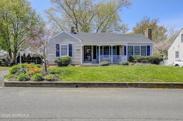 view of front of home featuring covered porch, a chimney, and a front yard