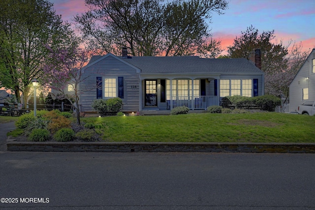 ranch-style house featuring a porch, a chimney, and a front lawn