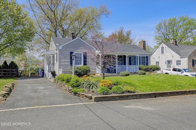 view of front facade featuring a porch, a front lawn, driveway, and a chimney