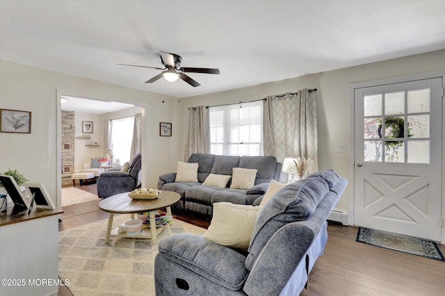 living area with plenty of natural light, a baseboard heating unit, ceiling fan, and wood finished floors