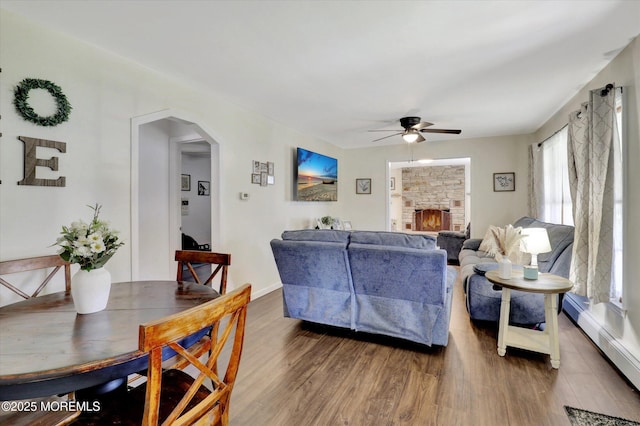 living area with wood finished floors, baseboards, ceiling fan, baseboard heating, and arched walkways