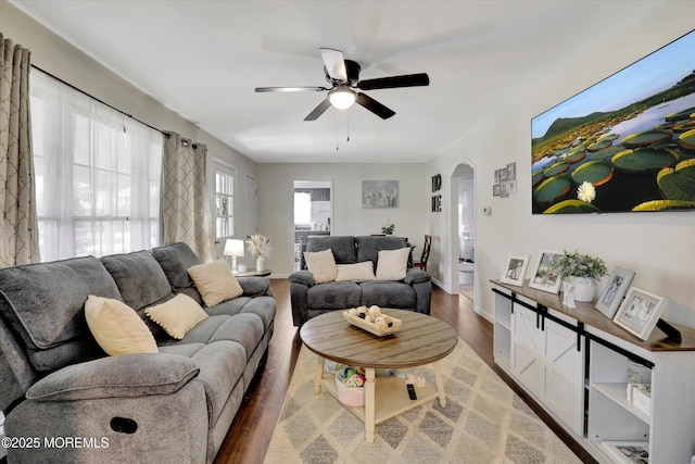 living area featuring baseboards, arched walkways, a ceiling fan, and wood finished floors