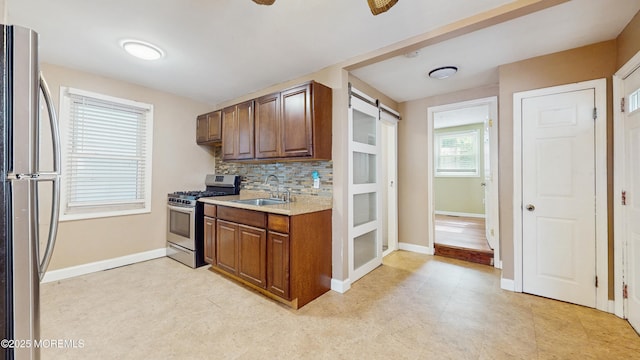 kitchen with decorative backsplash, a sink, light countertops, baseboards, and stainless steel appliances