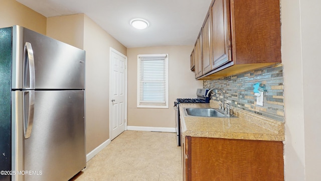 kitchen featuring baseboards, brown cabinets, tasteful backsplash, a sink, and appliances with stainless steel finishes