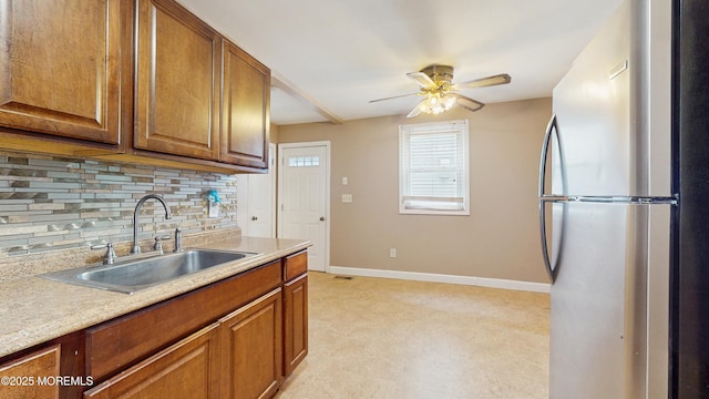 kitchen featuring freestanding refrigerator, decorative backsplash, baseboards, light floors, and a sink