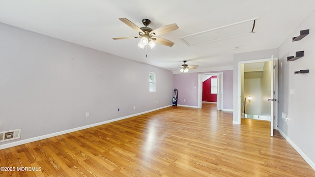 spare room with visible vents, baseboards, attic access, light wood-type flooring, and a ceiling fan