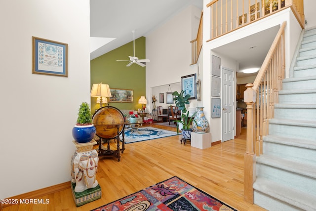 foyer featuring a ceiling fan, baseboards, stairs, high vaulted ceiling, and wood finished floors