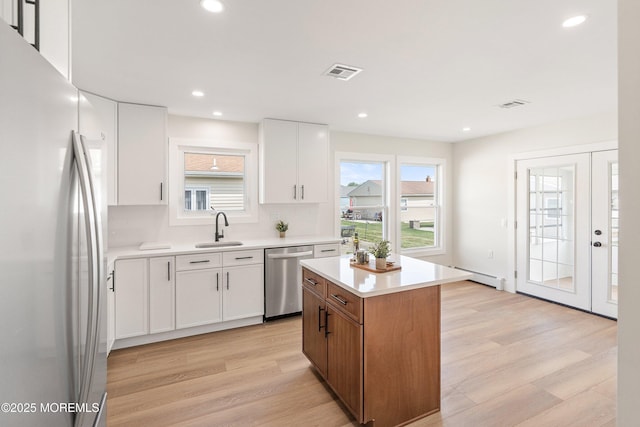 kitchen featuring visible vents, freestanding refrigerator, light wood-style floors, a sink, and dishwasher
