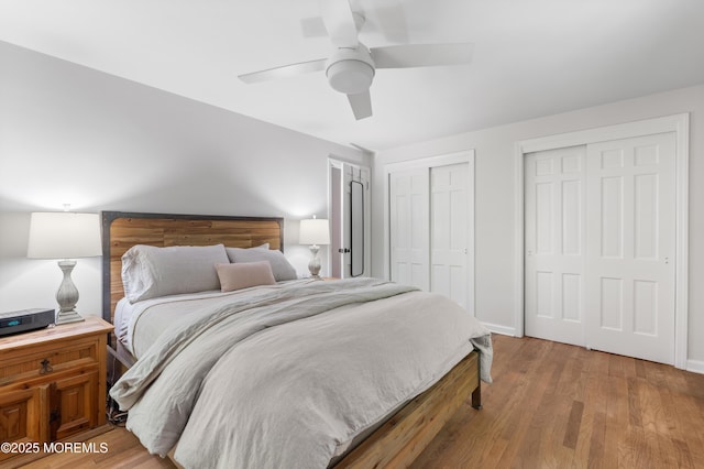 bedroom featuring baseboards, ceiling fan, two closets, and wood finished floors