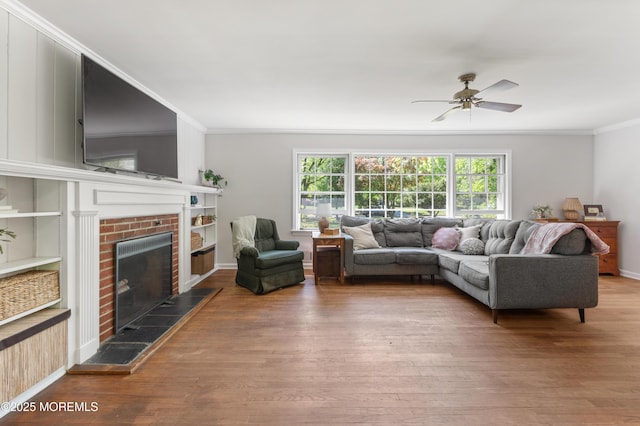 living area featuring a fireplace with raised hearth, ornamental molding, a ceiling fan, and wood finished floors