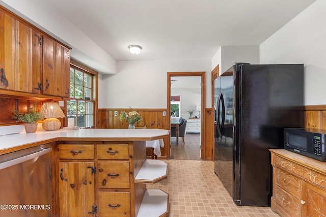 kitchen with brown cabinetry, light countertops, wainscoting, and black appliances
