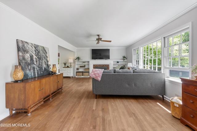 living room with ornamental molding, a brick fireplace, baseboards, a ceiling fan, and light wood finished floors