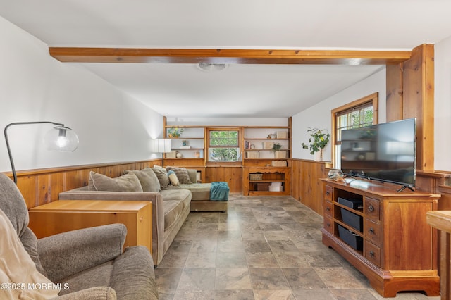 living room with wooden walls, a wainscoted wall, beamed ceiling, and stone finish floor