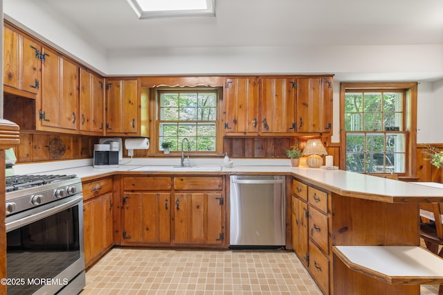 kitchen with a peninsula, light countertops, brown cabinets, a sink, and appliances with stainless steel finishes