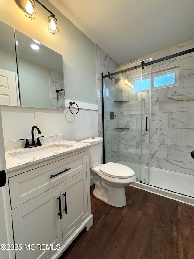 bathroom featuring vanity, toilet, wood finished floors, and a marble finish shower